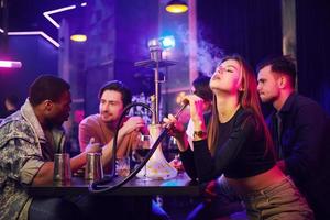 Woman smoking hookah. Group of friends having fun in the night club together photo