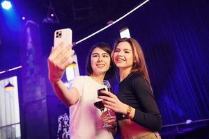 mujeres de pie en el club nocturno y haciendo selfie foto