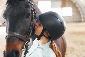 Kissing the animal. A young woman in jockey clothes is preparing for a ride with a horse on a stable photo