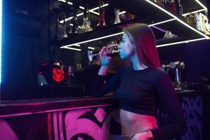 mujer joven de pie en el club nocturno con bebida en la mano foto