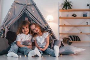 Embracing each other. Two little girls is in the tent in domestic room together photo