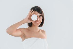 Holding cream for the skin care. Young brunette is indoors against white background photo