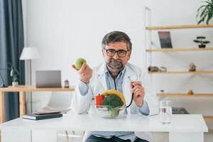 Conception of healthy eating. Man is sitting by the table. Professional medical worker in white coat is in the office photo