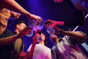 Holding glasses in hands. Group of friends having fun in the night club together photo