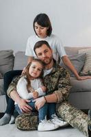 abrazándose unos a otros. soldado en uniforme está en casa con su esposa e hija foto