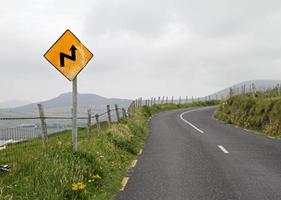 Yellow warning sign in front of a curve photo