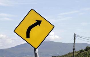 Yellow warning sign in front of a curve photo