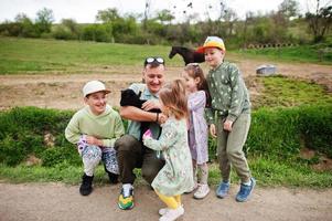 padre con cuatro hijos en una granja ecológica de animales sostenga un cordero de oveja bebé en la mano. foto