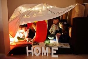 Playing kids with kitty in tent at night home. Hygge mood. photo