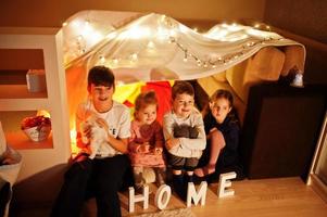 jugando a los niños con el gatito en la carpa por la noche en casa. estado de ánimo hygge. foto