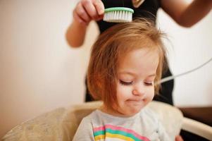 mamá con hija haciendo juntos la rutina diaria. la madre está cepillando y secando el cabello del niño después de la ducha. foto