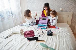 madre e hijas maquillándose en la cama del dormitorio. foto