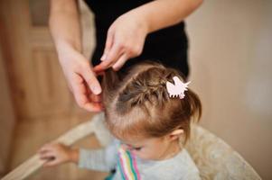 Mother and daughter weekend together at home, mom making hairstyle for baby girl. photo