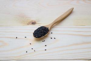 Black sesame seeds in wooden spoon pile on wood table photo
