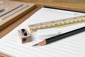 lápiz, borrador, regla con libro sobre mesa de madera foto