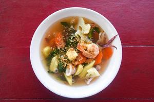 Thick Gravy seafood noodles with squid shrimp prawn and vegetable on bowl on red wooden table photo