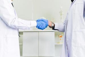 Doctor and scientist shaking hands with her colleague healthcare and cooperation or the success of the research trial scientific concept - Male scientist are shaking hand in laboratory photo