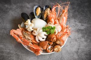 Seafood shrimps prawns squid mussels spotted babylon shellfish crab  on plate and dark background - Cooked food served seafood buffet concept photo