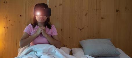 Young woman using virtual reality headset in bed. VR, Future digital technology, game, movies entertainment, metaverse, NFT and 3D cyberspace concept photo