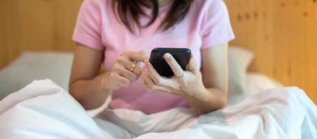 woman using smartphone for social media, young female watching movies by mobile phone on bed at home. technology, network, online shopping, e commerce, lifestyle and digital communication concept photo