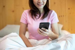 mujer que usa un teléfono inteligente para las redes sociales, una mujer joven que ve películas por teléfono móvil en la cama en casa. tecnología, red, compras en línea, comercio electrónico, estilo de vida y concepto de comunicación digital foto