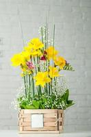 A vertical shot of a beautiful composition with daffodils and pink freesia in a wooden box photo