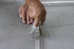 Hand of worker holding a wheel tool to install a aluminum mosquito net wire mesh screen this is to be attached to the window of the house to prevent insects. photo