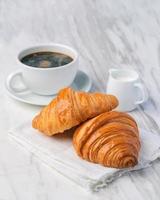 croissants recién hechos, pan y una taza de café sobre tela. desayuno francés foto