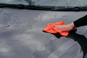 Cleaning car using microfiber cloth. Man washes black auto hood. Polishing vehicle. Car detailing, maintenance photo