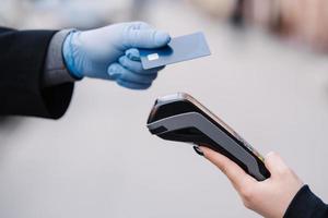 Faceless human in medical gloves during coronavirus epidemic, holds plastic card, tries to makes cashless payment for safety, uses modern technology. Pandemic, virus and prevention concept photo