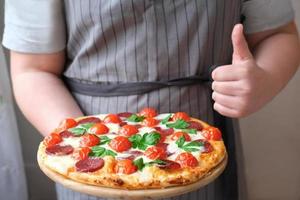 niño adolescente sosteniendo pizza y mostrando el pulgar hacia arriba. foto