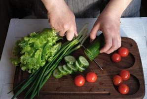 woman in grey apron cuttting vegetables for salad. photo