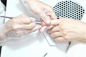 manicurista profesional empujando la cutícula en la mano femenina foto
