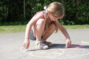 happy little girl drawing with chalk on the pavement. photo