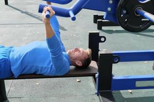 sporty slim man doing bench press using outdoors gym equipment. photo