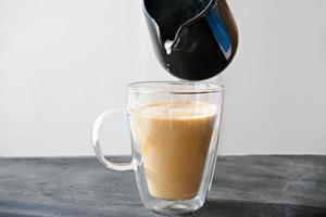 mano sosteniendo una jarra de leche y vertiendo leche en una taza de café foto