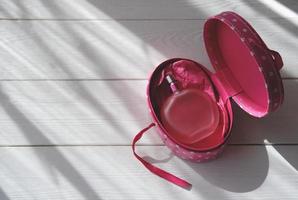 botella de perfume rosa sobre fondo blanco de madera con luz directa. foto