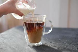 la mano de una niña sosteniendo un vaso de leche y vertiendo leche en una taza de café. foto