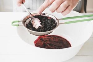 making berry puree. Woman strains berries through a sieve photo