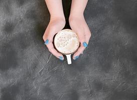 manos de mujer con manicura azul sosteniendo una taza de café caliente foto