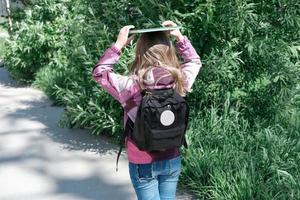 niña yendo a la escuela con mochila y un libro en la parte superior de la cabeza. foto