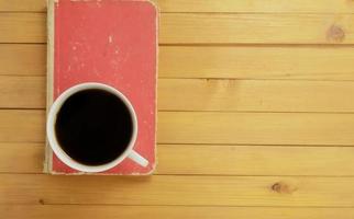 Top view, A cup of coffee and closed red book on wooden background photo