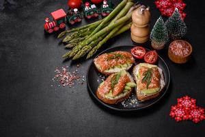 sándwich tostado con mantequilla, aguacate y salmón, decorado con rúcula y semillas de sésamo, en una mesa navideña foto