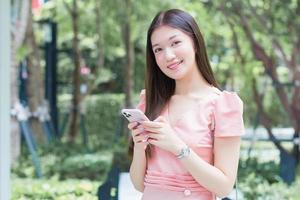 Asian professional  business female with long hair is smiling in the garden while looking at the smartphone in her hand, work from anywhere concept. photo