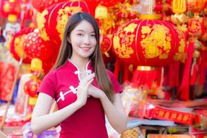 Beautiful Asian woman with long hair who wears a red Cheongsam dress in Chinese new year theme while she shows her hand as Chinese greeting with a red Chinese lantern festival as a background. photo