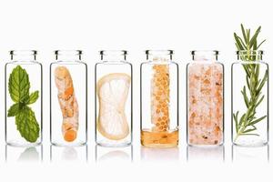 la botella de vidrio de cuidado de la piel casero y exfoliaciones corporales con ingredientes naturales sal del himalaya, menta, romero, cúrcuma y miel aislada sobre fondo blanco. foto