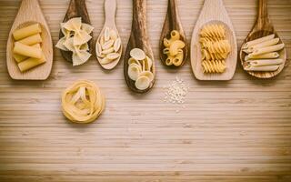 Italian foods concept and menu design. Various kind of Pasta Farfalle, Pasta A Riso, Orecchiette Pugliesi, Gnocco Sardo and Farfalle in wooden spoons setup on bamboo cutting board with flat lay. photo