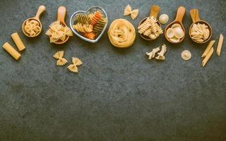 Italian foods concept and menu design. Various kind of Pasta Farfalle, Pasta A Riso, Orecchiette Pugliesi, Gnocco Sardo and Farfalle in wooden spoons setup on stone background with flat lay. photo