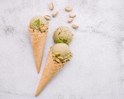 Pistachio ice cream in cones with pistachio nuts setup on white stone background . Summer and Sweet menu concept.