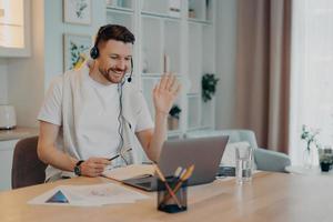 Happy young guy in headphones working from home and using online communication photo